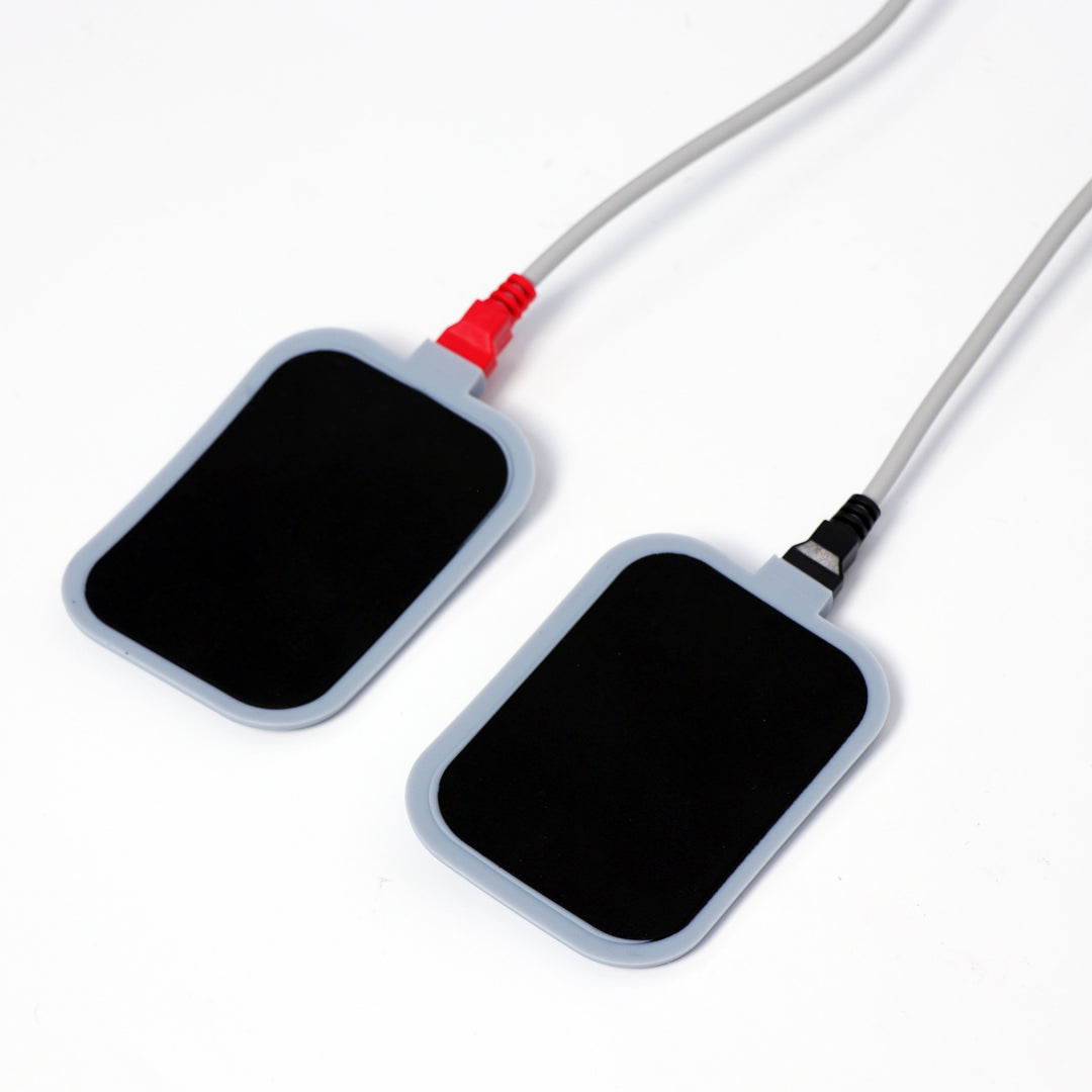 Pair of rectangular body treatment electrode pads with red and black connector cables for professional aesthetic machine treatments.